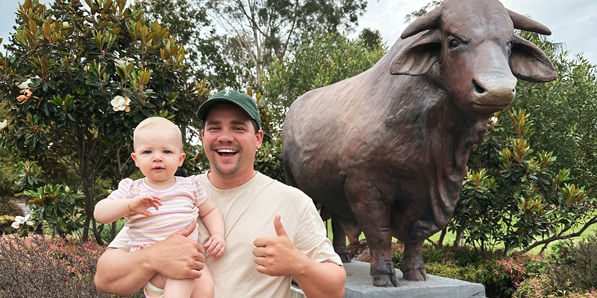 A man holding a baby having a selfie with a bull statue