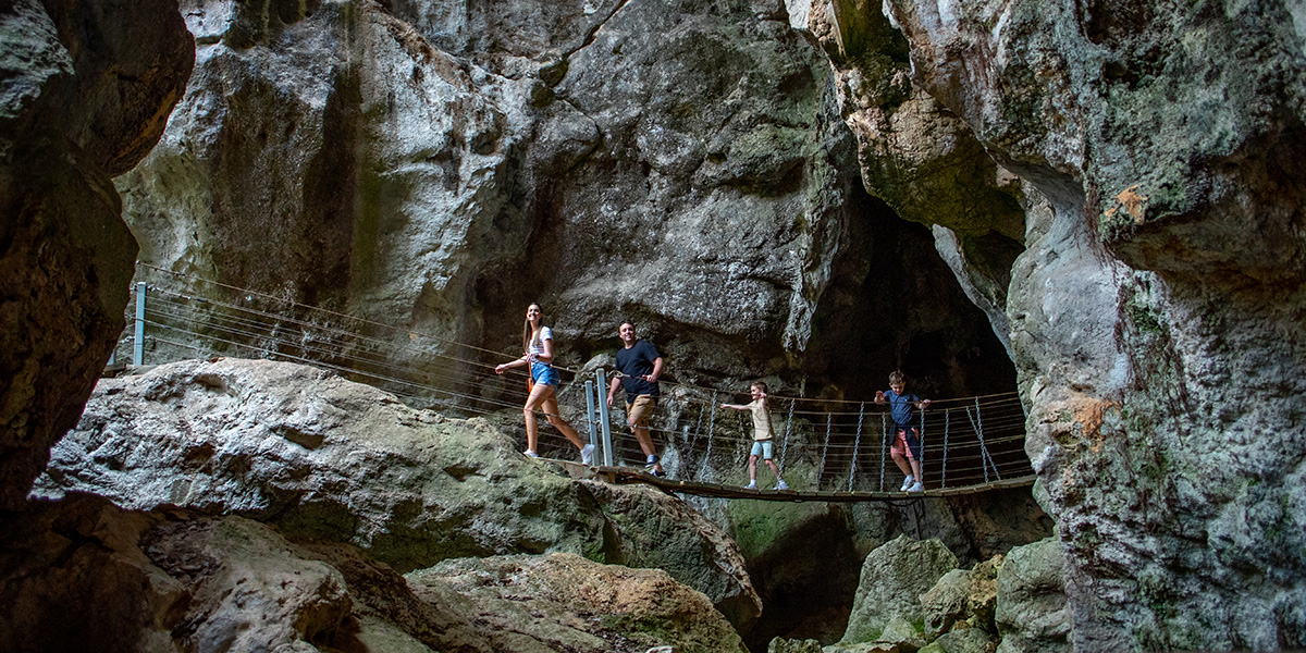 A family crossing a swinging bridge at the caves