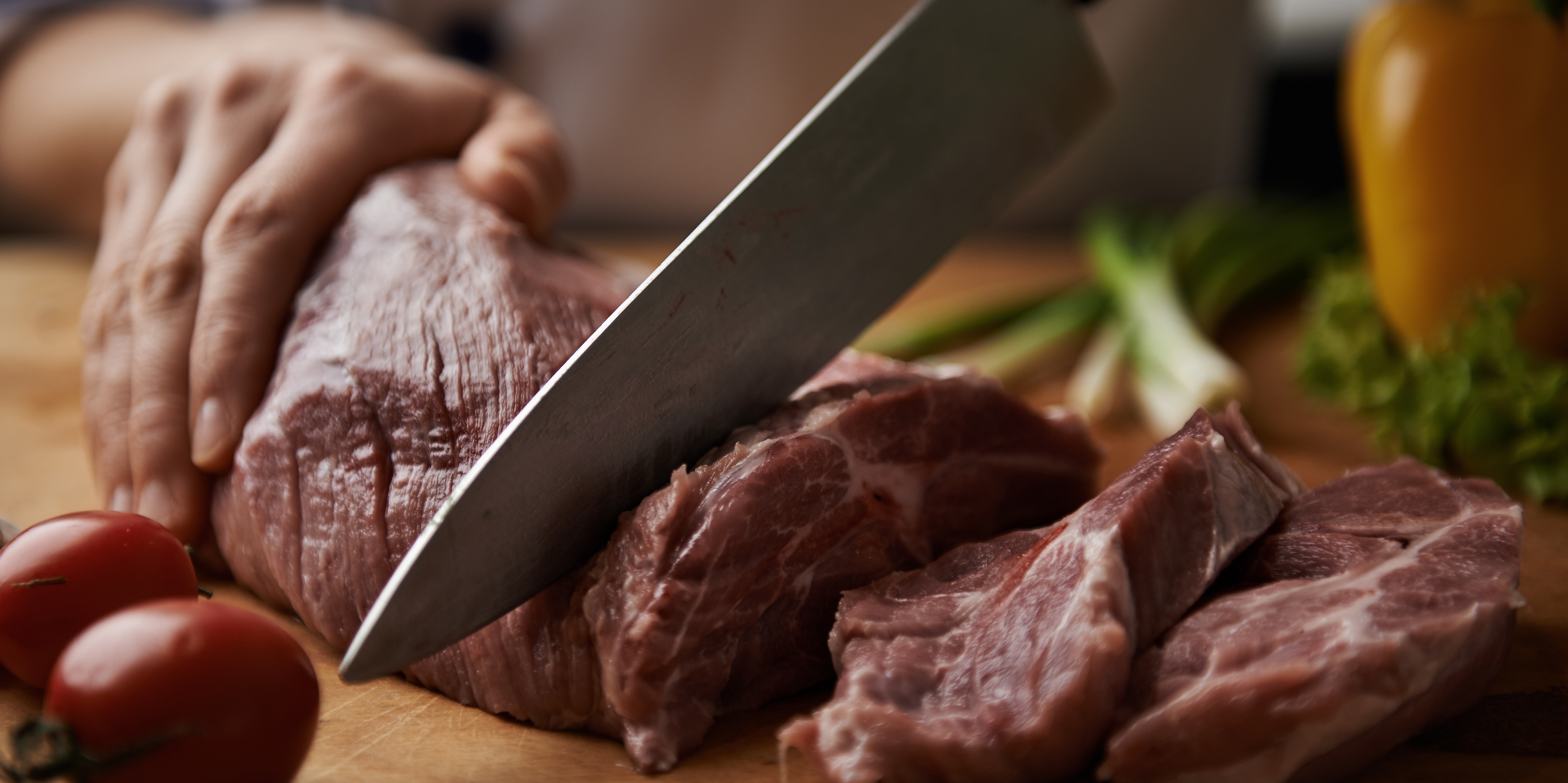 Close up of a raw piece of beef being carved up by a butcher knife