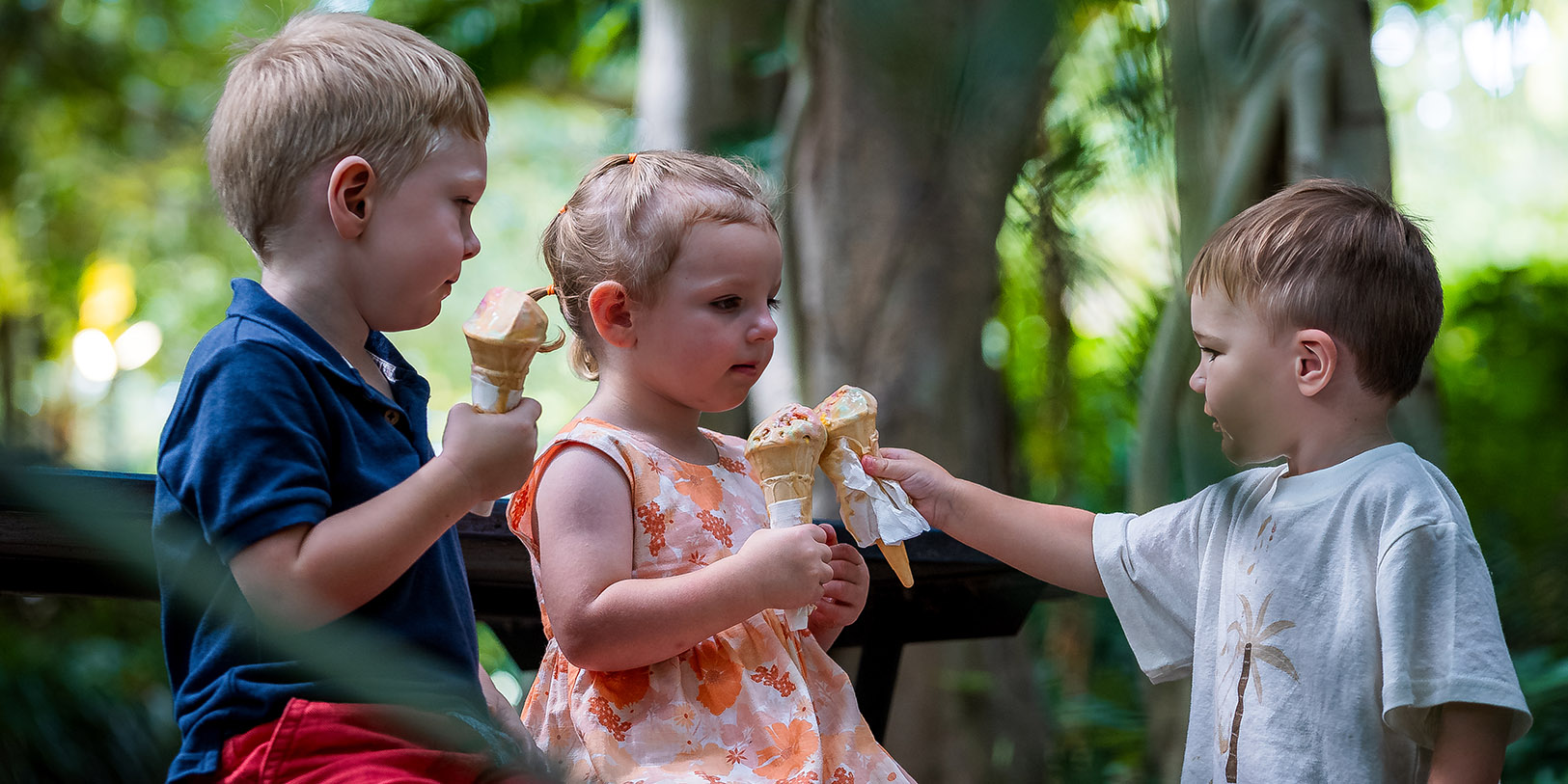 Thee young children enjoying ice cream in a lush garden setting.