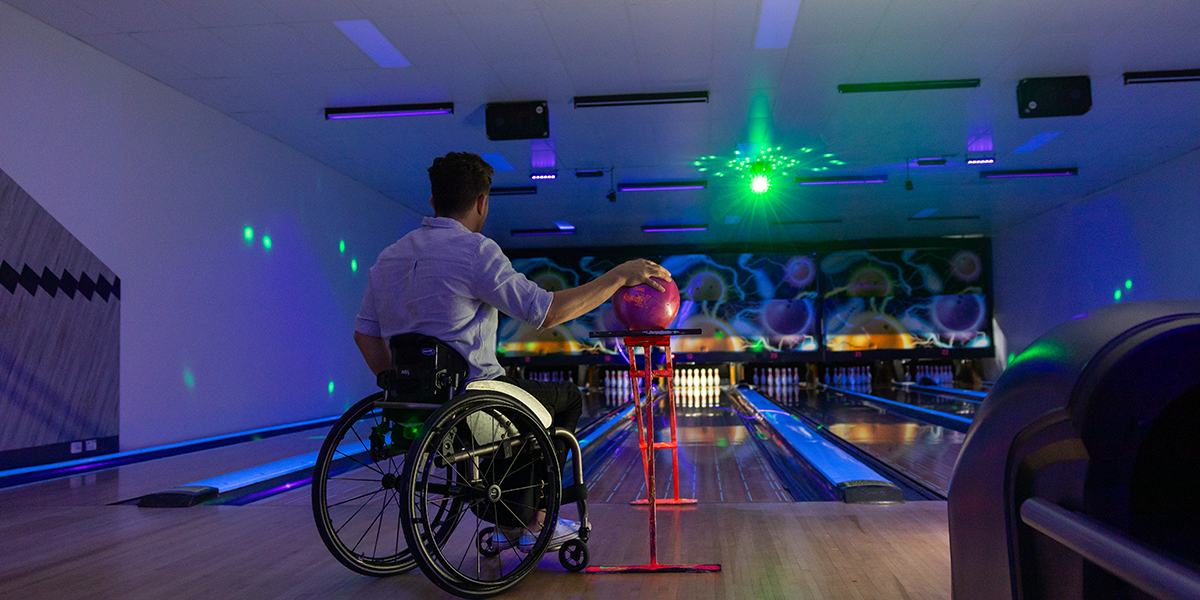 A man in a wheel chair about to bowl a strike at ten pin bowling.