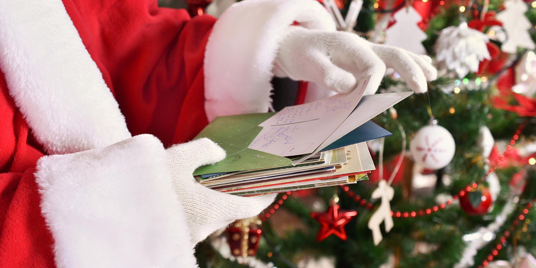 Close up of Santa Claus' gloves holding a handful of letters from children who have written to him with their Christmas wishes.