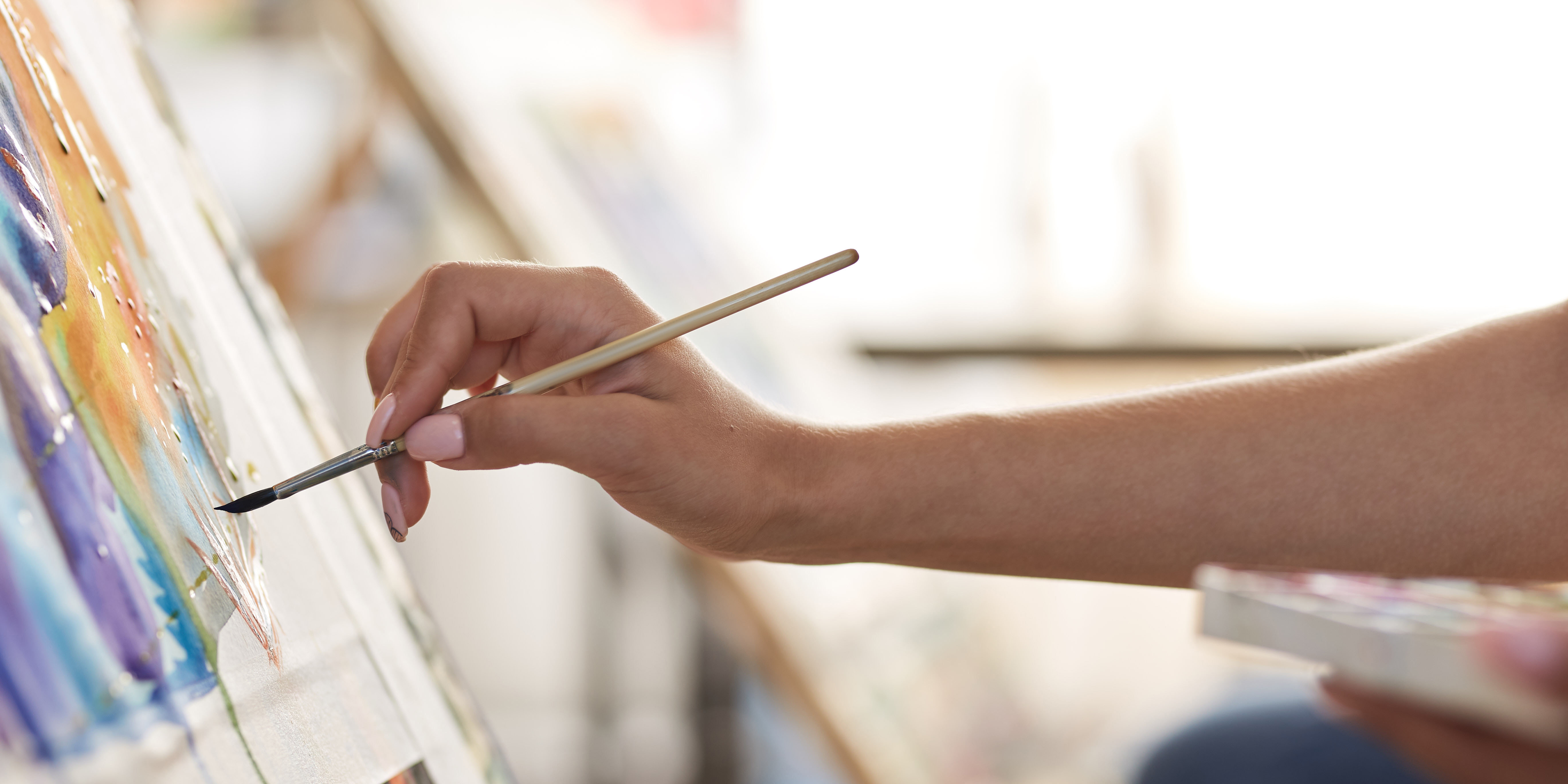 right hand holding paint brush reaching out to paint on canvas