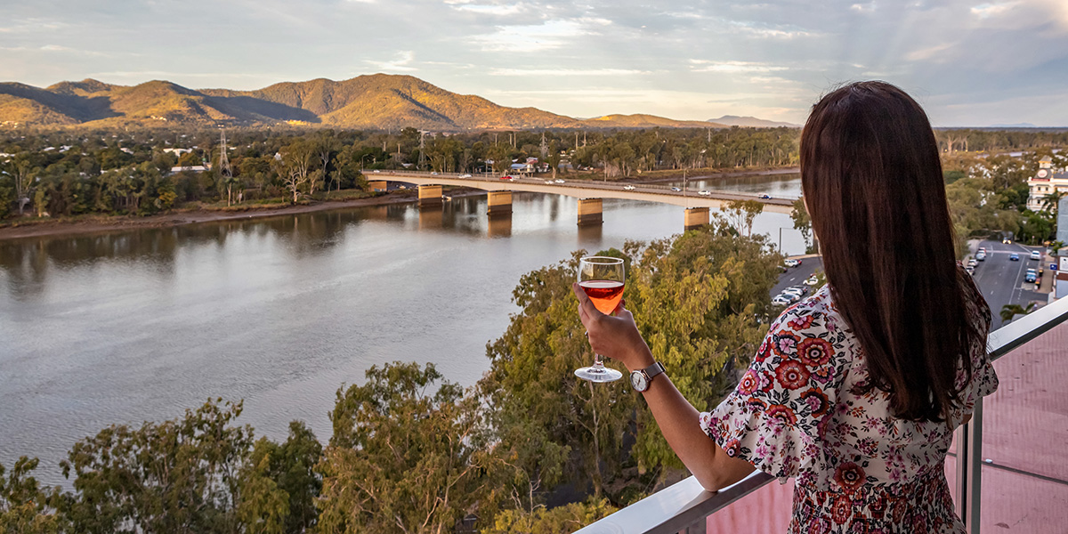a woman drinking wine on a balcony looking at the river