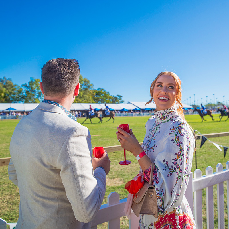 Glamourously dressed couple watching Pop up Polo in Rockhampton with horses in background