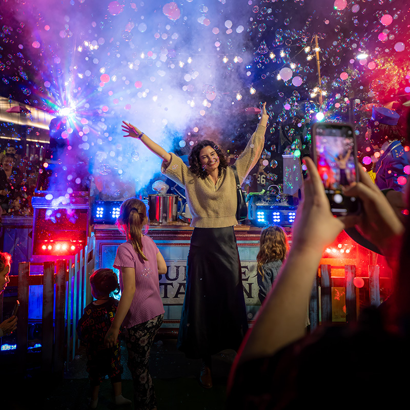 Woman in front of a stage of bubbles and lights at night with her arms up at Rockhampton River Festival